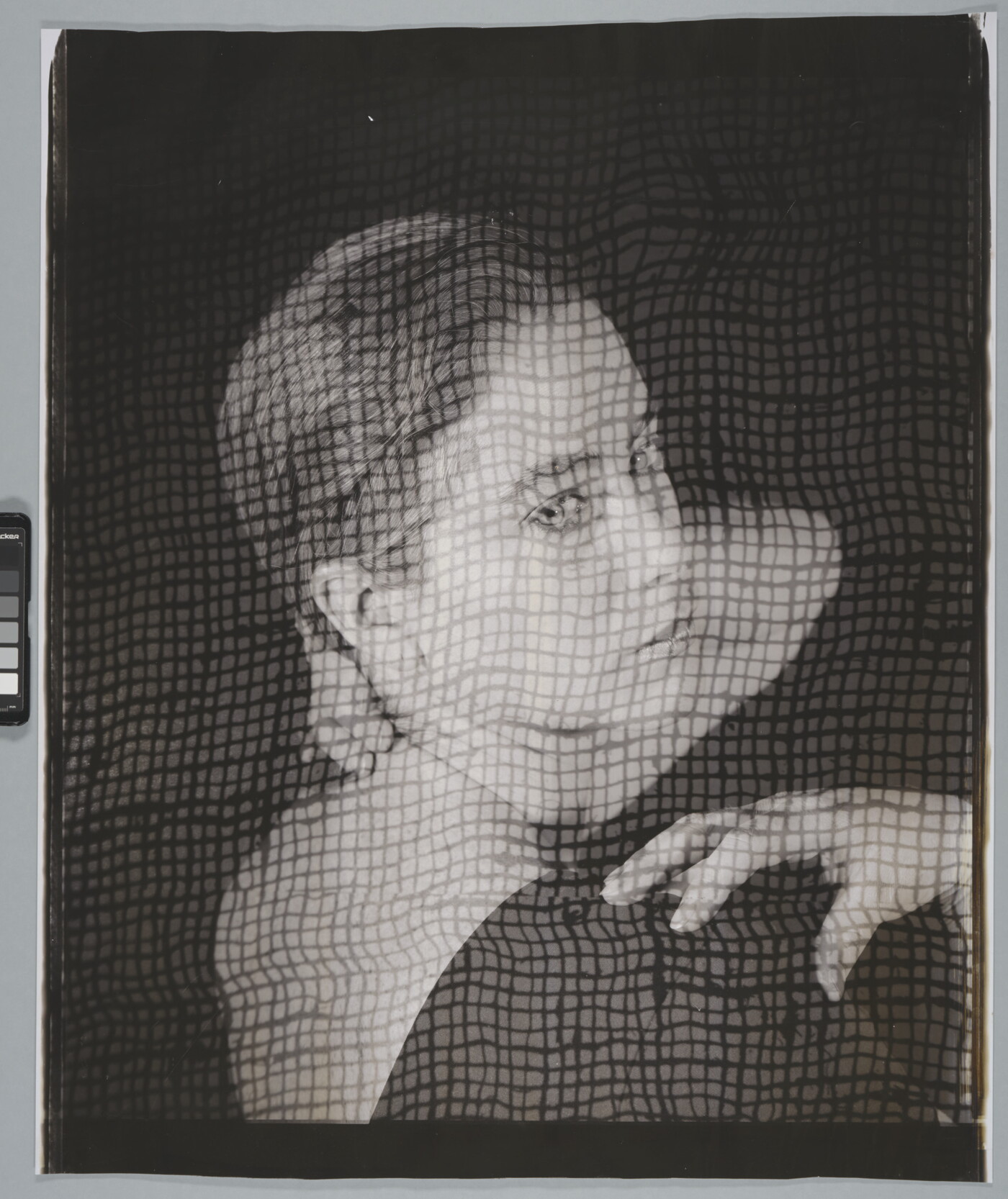 A black-and-white portrait photograph of a White woman, head turned to look over her shoulder, as viewed through what looks like a screen.