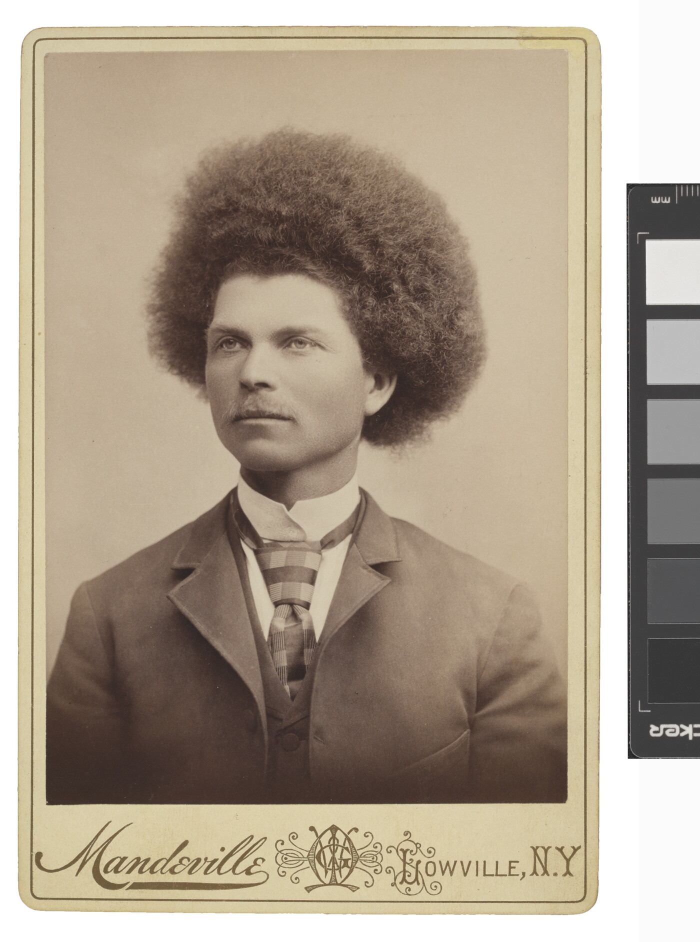 A sepia-toned studio portrait photograph of a man with &quot;Afro&quot;-style hair wearing a suit, collared shirt, vest, and tie.
