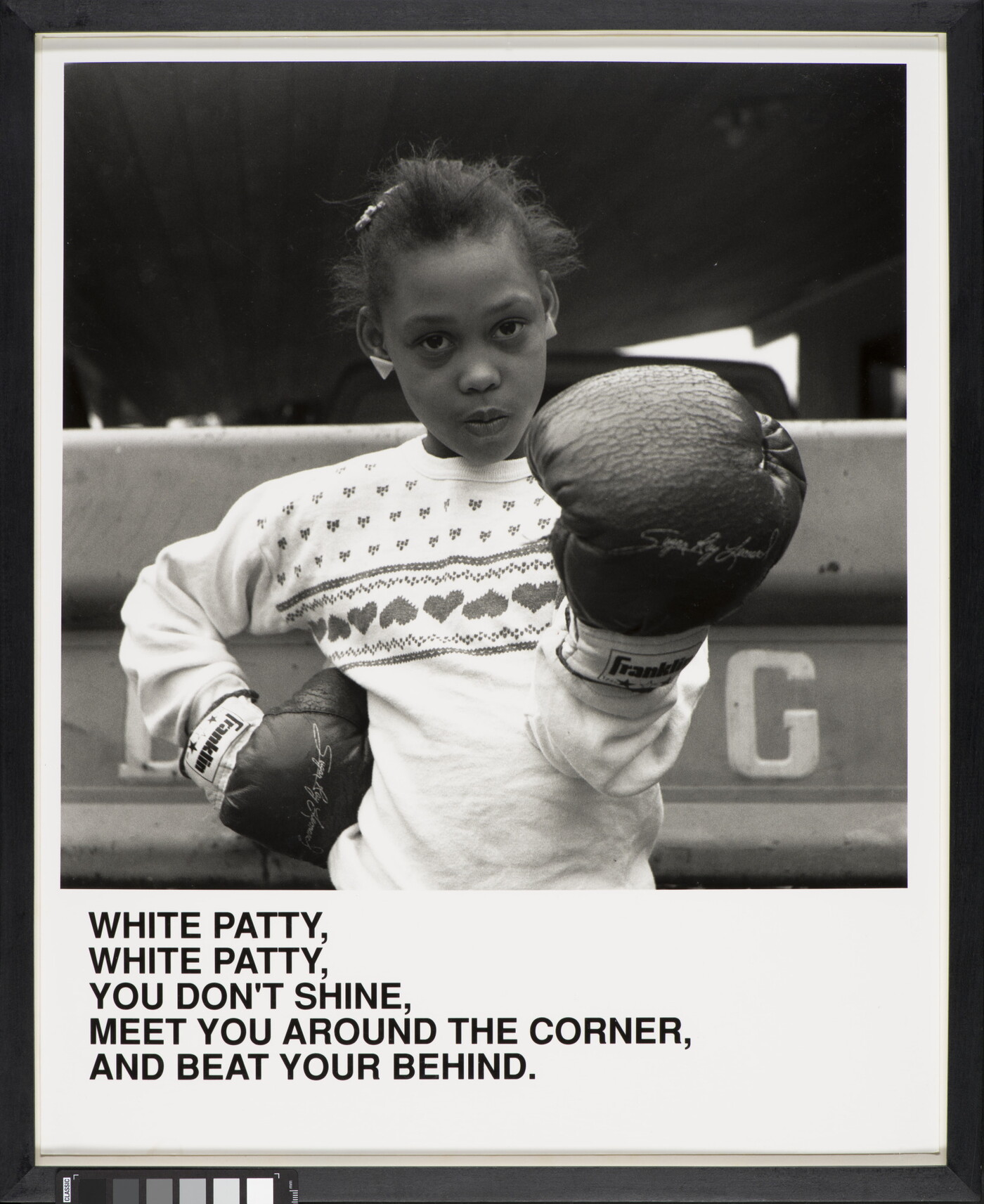 A black-and-white photograph of a Black girl wearing boxing gloves and looking at the camera above text that reads, &quot;White Patty, White Patty, You don&#039;t shine. Meet you around the corner and beat your behind.&quot;