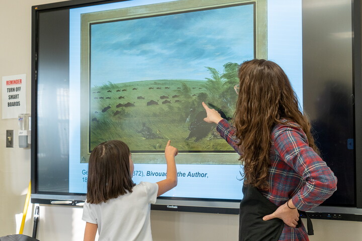 A child points to a detail in an artwork on a screen as a Carter educator watches.