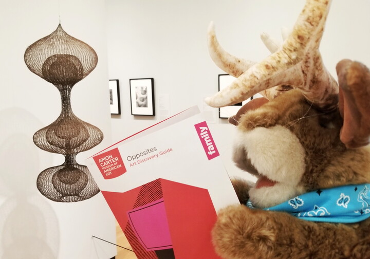 A jackalope puppet holds an Art Discovery Guide while looking at art in a Carter gallery.