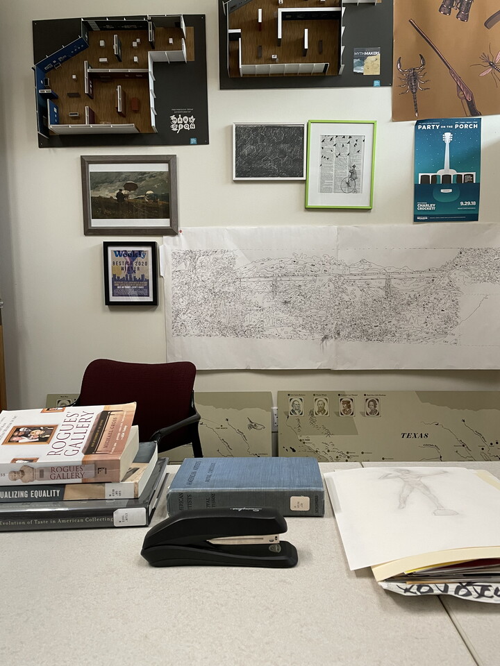 An office desk with stacked library books, manilla file folders, and a black Swingline stapler.