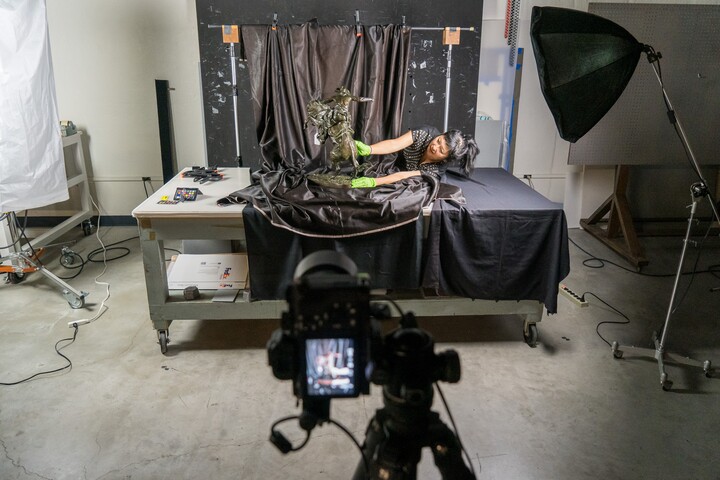A camera's viewfinder frames artist Stephanie Syjuco arranging a sculpture on a table for a photoshoot.