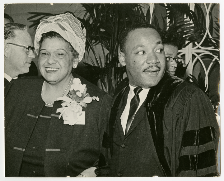 A black-and-white photograph of a Black woman and a Black man in a crowded room.