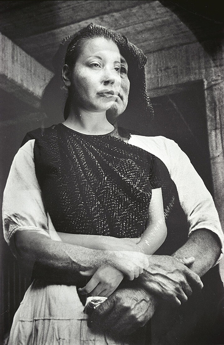 A black-and-white double-exposed photograph of two women, one in modern clothing and the other in traditional clothing, standing with their arms folded in front of their waist.