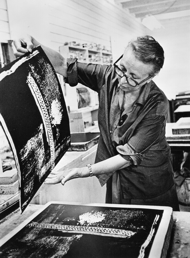A woman lifts a print off of a lithography stone.