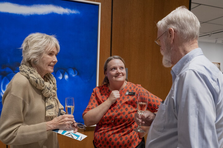 A White woman talks to two older adults in front of a painting in a Carter gallery.
