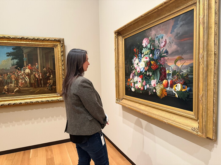 A White woman with long dark hair looks at a floral still life painting in a Carter gallery.