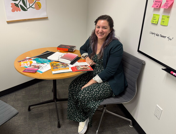 A smiling White woman sits at a table covered with brochures, magazines, and other Carter collateral.