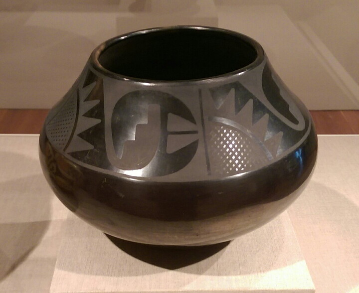 A shiny black pot with Native American designs on the top half in a matte black.