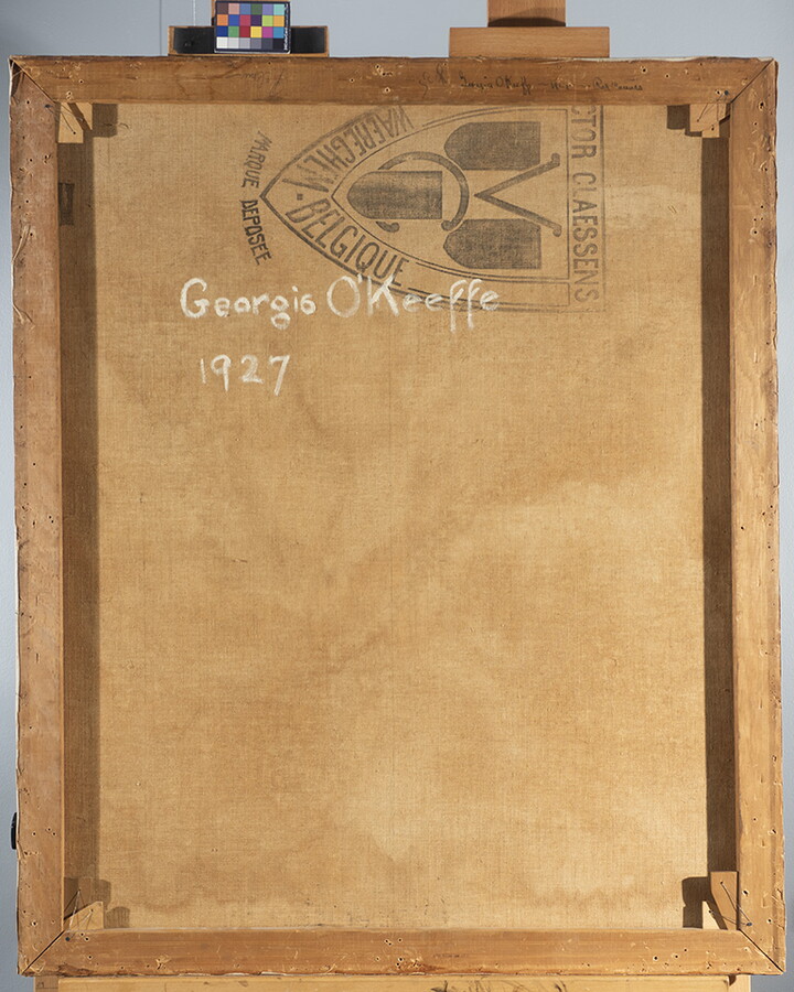 The back of a painting showing a manufacturer stamp and, handwritten in white, "Georgia O'Keeffe, 1927."