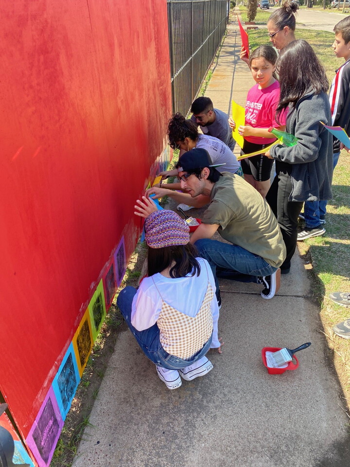 A man works with a group of preteens on a mural next to a sidewalk.