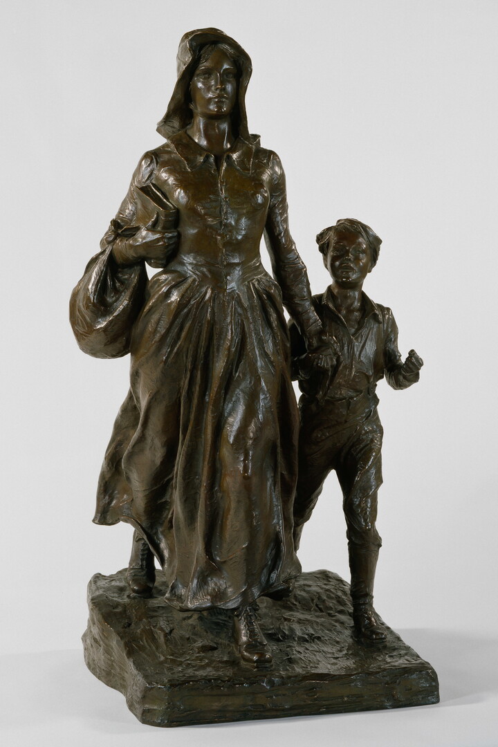 A bronze sculpture of a woman wearing pioneer clothing holding the hand of a young boy.