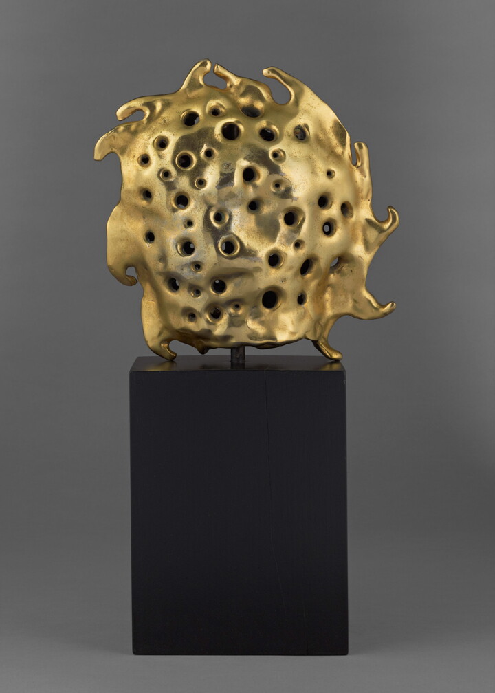 A bronze sculpture of a gold sun sitting atop a tall, dark rectangular base.