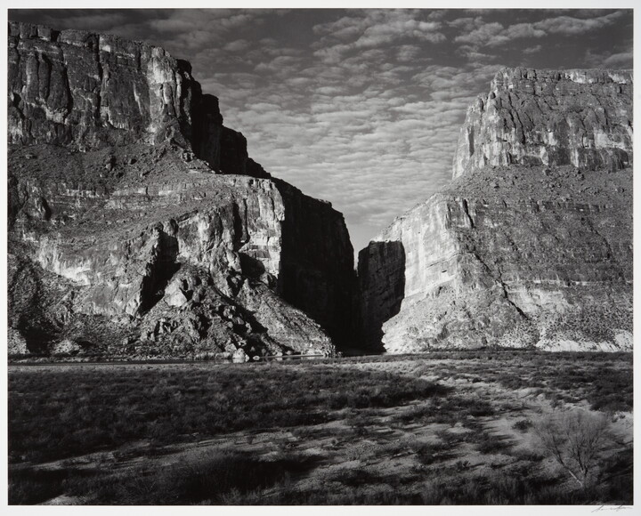A black-and-white photograph of a canyon between two large mountains.