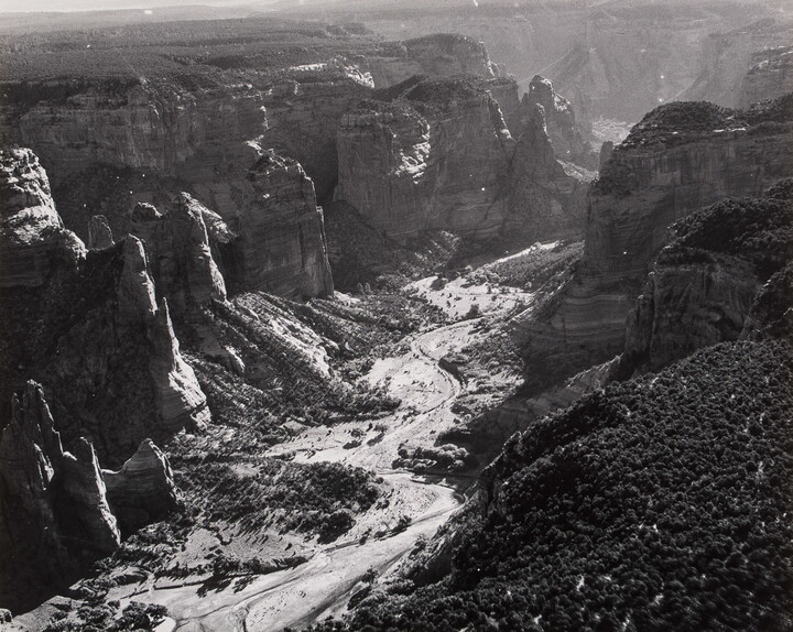 A black-and-white photograph of a landscape with two sides of steep and rocky cliffs and a dry valley between them.