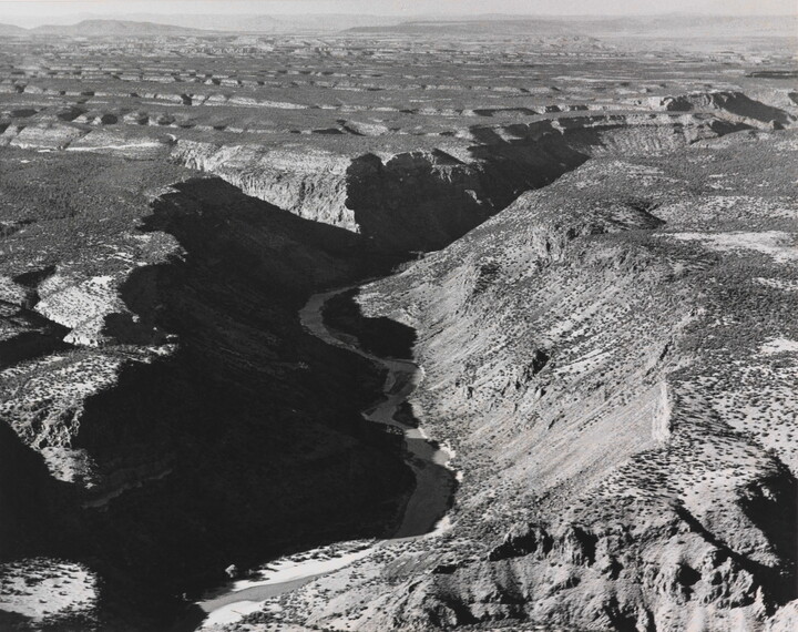 A black-and-white photograph of an aerial view of a river winding through a steep canyon.