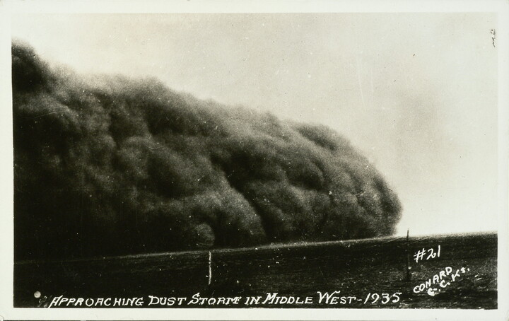 A black-and-white postcard photograph of a large dust storm rolling over an open landscape.