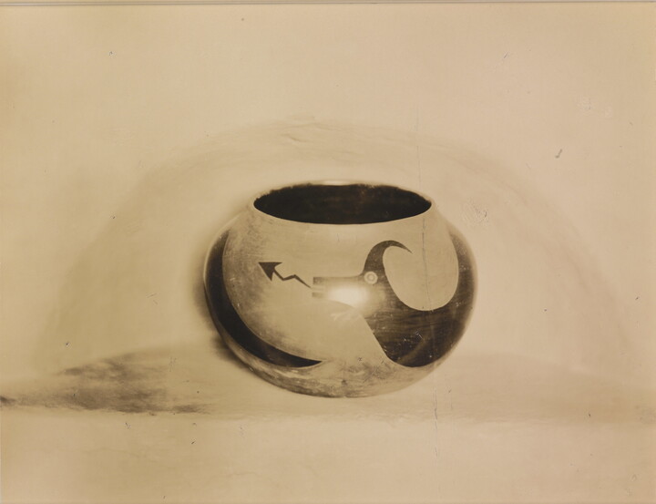 A sepia-toned photograph of a spherical bowl with abstract animal designs on a light background.