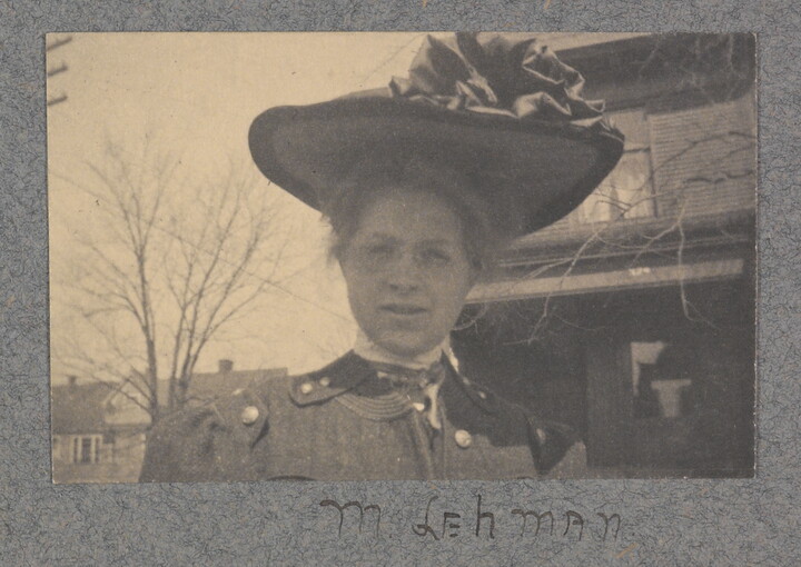 A black-and-white photograph of a White woman from the shoulders up, wearing a large brimmed hat with ruffles on top.