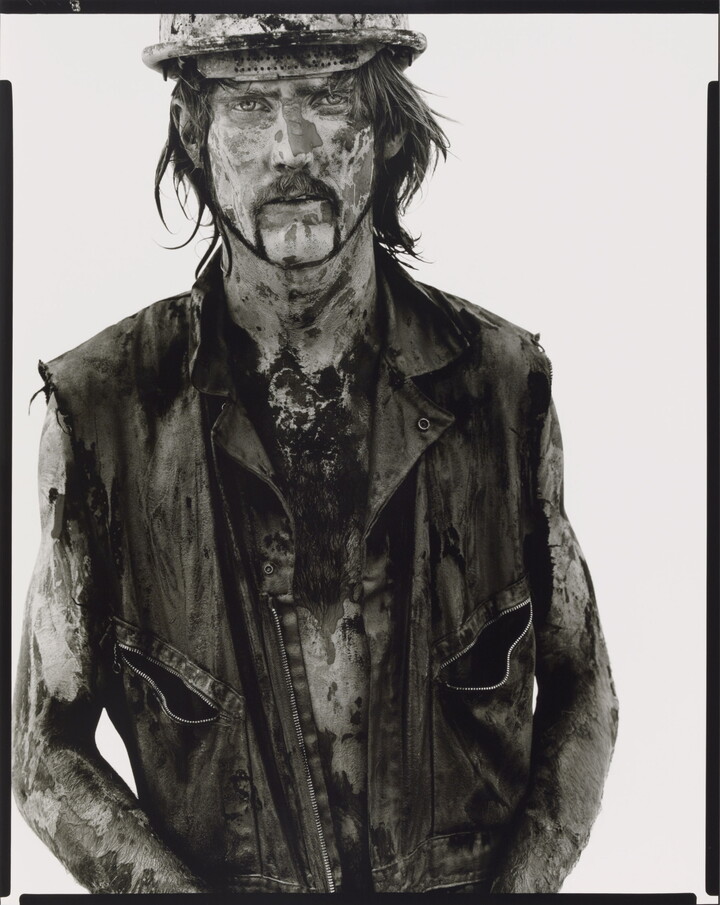 A black-and-white portrait photograph of a White man covered in dirt and oil wearing a vest and hard hat.
