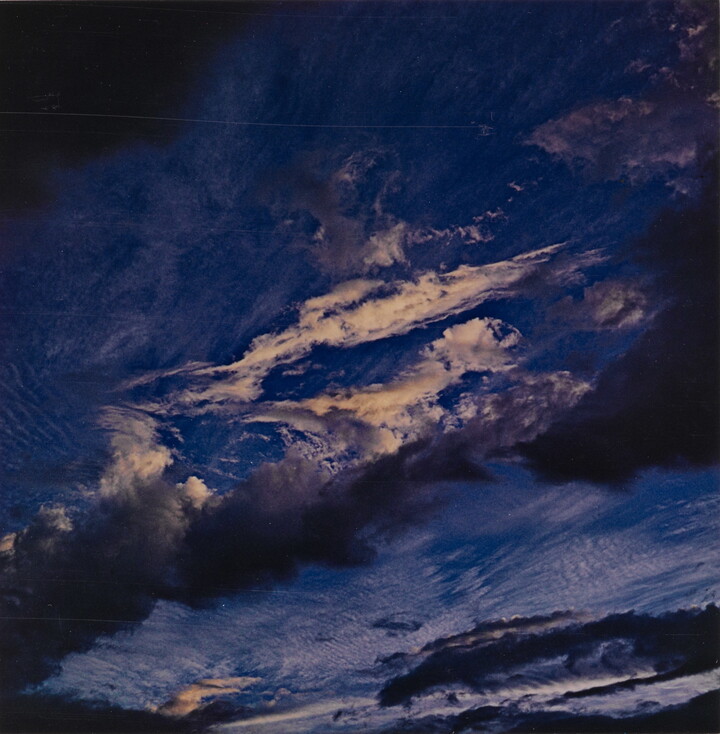 A color photograph of a dark blue sky streaked with dark and light clouds.