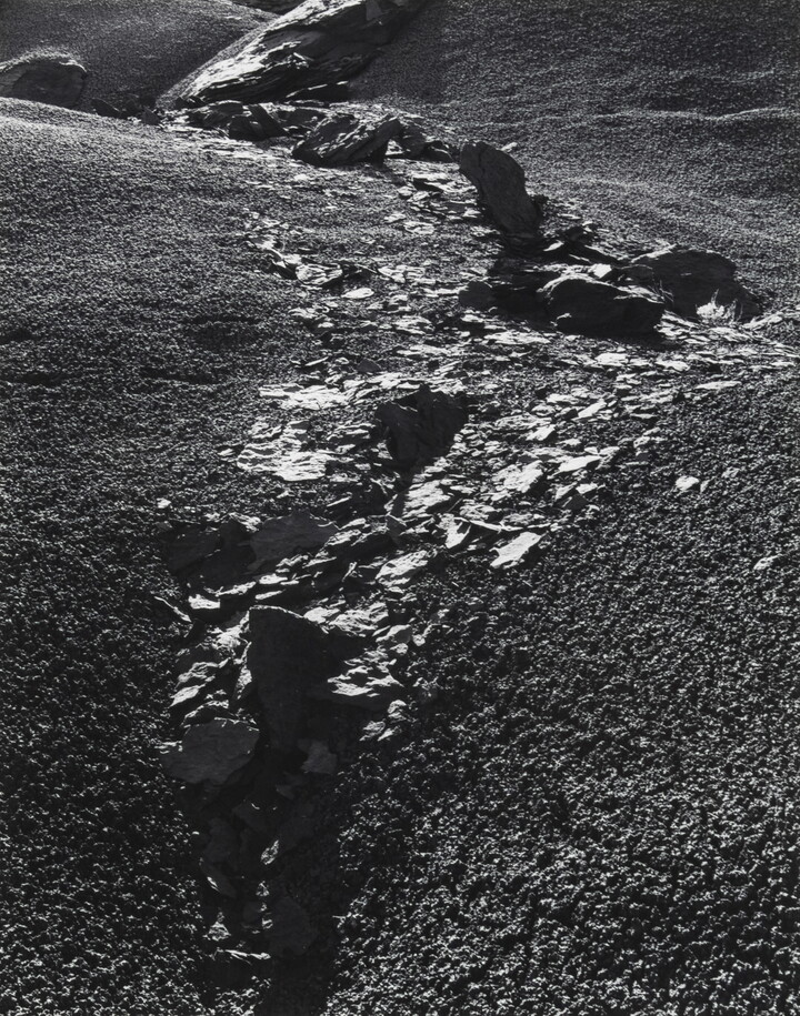 A black-and-white photograph of rocks and rock flakes bisecting a gravelly slope.