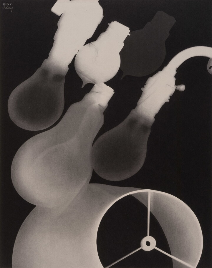 A black-and-white photograph of four incandescent lightbulbs placed diagonally above a lampshade.