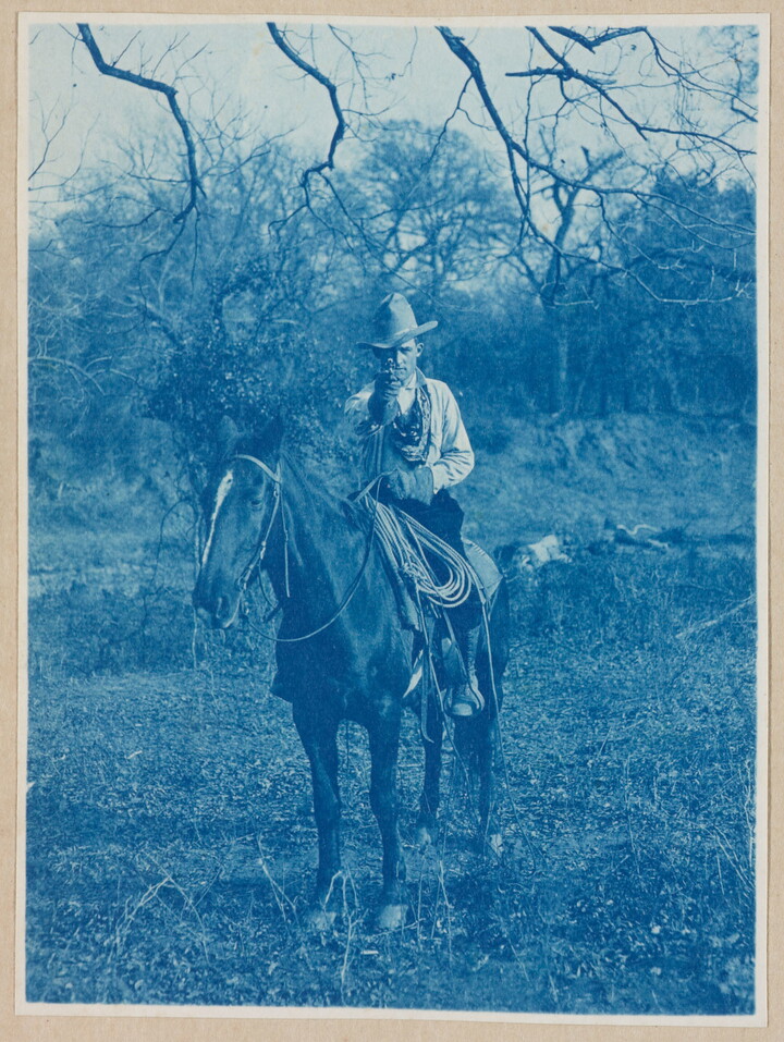 A black-and-white photograph of a man wearing a cowboy hat on horseback, pointing his revolver toward the viewer.