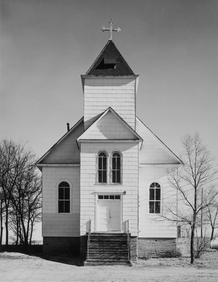 A black-and-white photograph of a white clapboard church with a cross atop the steeple.