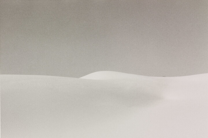 A black-and-white landscape photograph of a white sand dune against a gray sky.
