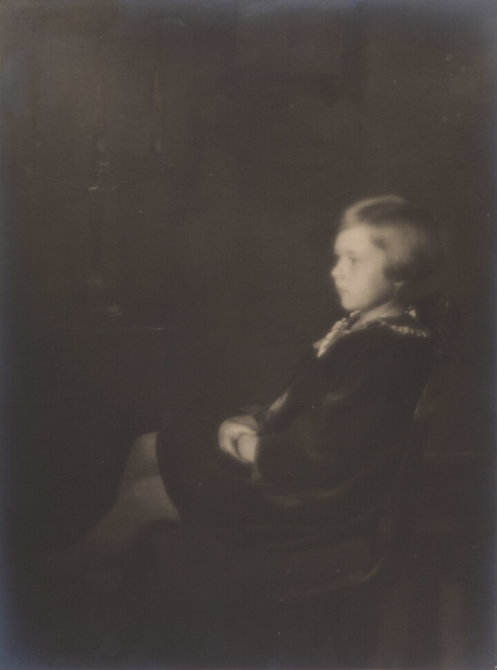 A black-and-white, soft-focus photograph of a young White girl with bobbed hair, sitting in profile.