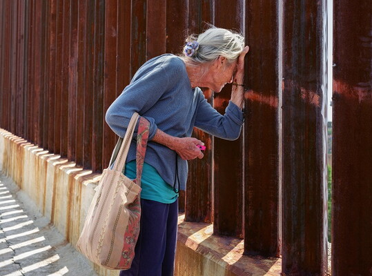 Older woman leans forward to look through rusted bars