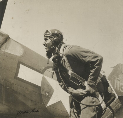 A black-and-white photograph of a Black man wearing a pilot uniform, including a helmet with goggles pushed up on his head, standing in front of an airplane.