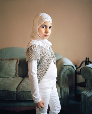 A color photograph of a light-skinned pre-teen girl, dressed all in white, including a headscarf over her head.