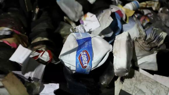 A video still of garbage, including plastic bottles, paper, Styrofoam.
