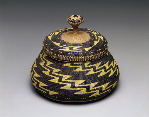 A woven basket and lid with a yellow and black zig-zag pattern.