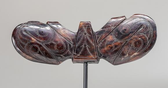 A dark brown sculpture that resembles a winged insect, with white designs carved into it.