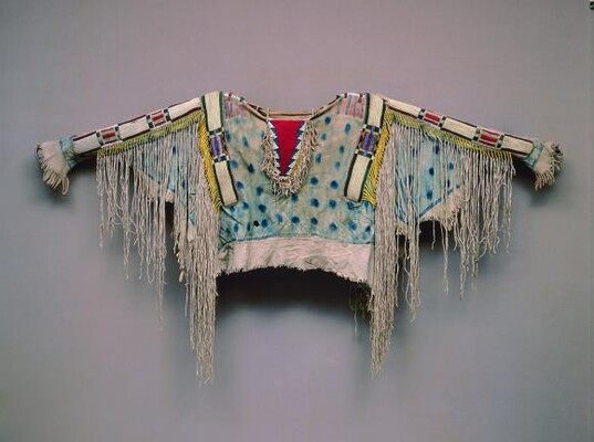 A elaborately decorated shirt with long white fringe, a blue bodice with dark blue dots, and sleeves with beaded designs.