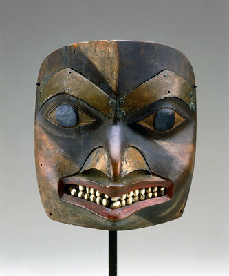 A wood and metal mask of a stylized human face complete with grinning mouth and white teeth.