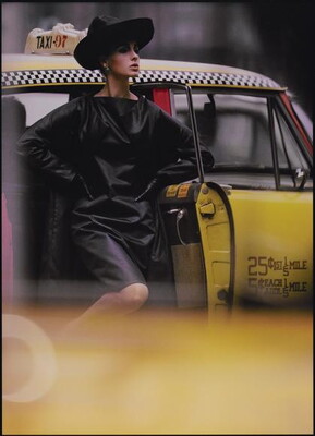 A color photograph of a White woman in a black hat and black leather dress stepping out of a taxi.
