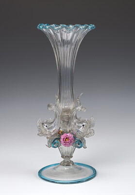 A decorative glass vase, curved in a trumpet-like form with three dolphins and three flowers along the base.