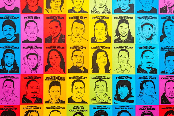 A detail of an installation: head and shoulder portraits of many people of color under their names printed on colored paper.