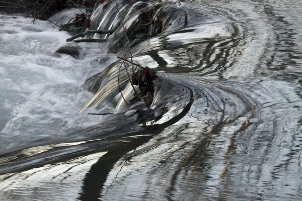 A close-up color photograph of water swirling off a rock ledge into a deeper pool.