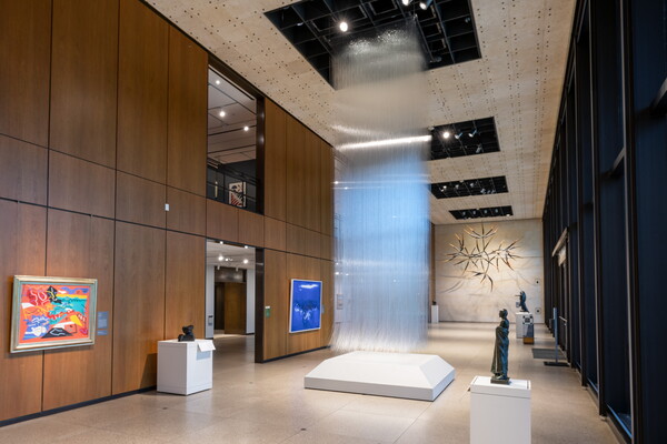 An installation view of a sculpture made of thousands of clear, glass threads hanging from the ceiling of a Carter gallery.