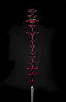 A vertical red, metal sculpture of a sound wave composed of a stack of different sized discs.