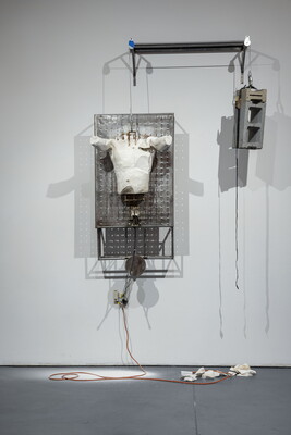 A plaster cast of a male torso hangs from a cable and pulley balanced by concrete bricks on the other end of the cable.