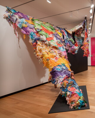 Layers of brightly colored tissue paper cascade over a wall to a point on the floor of a Carter gallery.