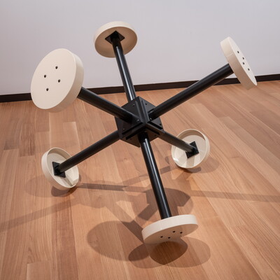 A large metal sculpture, shaped similar to a toy jack, with six black spikes each capped with a cream disc.