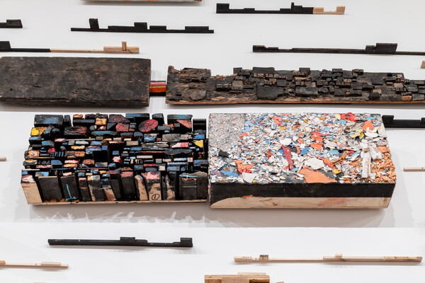 A detail of 3D wooden constructions with varied colors and textures mounted on a white wall.
